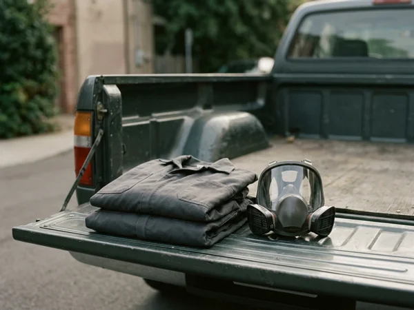 Neutral coveralls and full-face respirator resting on a tailgate