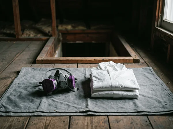 P100 particulate respirator and disposable coveralls laid out before an attic entry