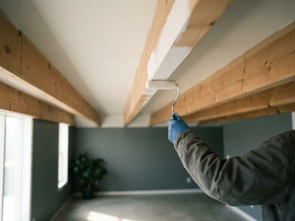 Roller applying shellac-based primer sealer to a bare ceiling joist