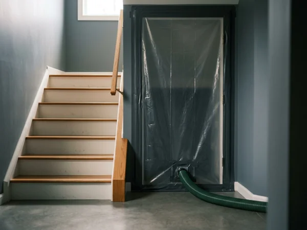 Sealed containment doorway with negative air hose at a basement stairwell